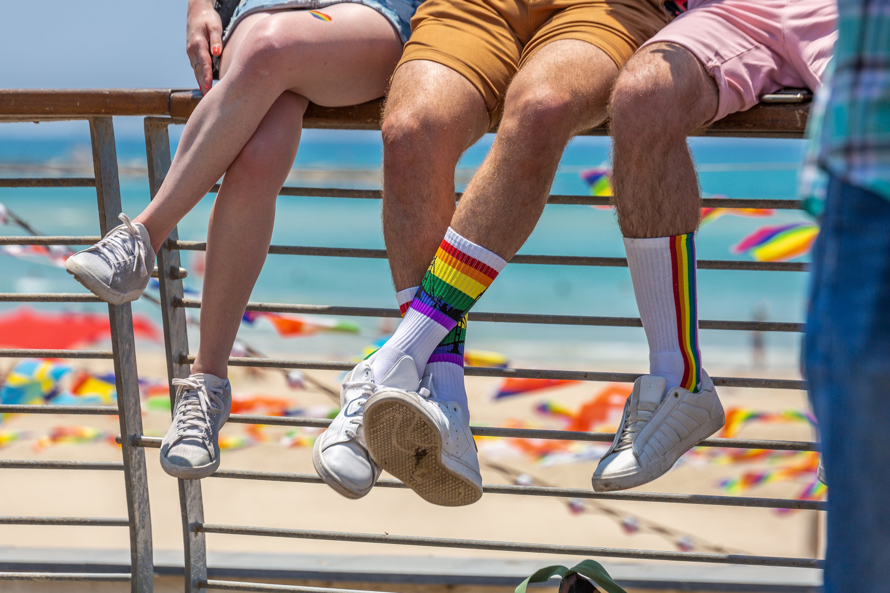 Close-up of three friends sitting on a boardwalk rail wearing rainbow pride socks and casual summer outfits, representing Supr Bueno’s inclusive, LGBTQ+ friendly web design studio that celebrates diversity, creativity, and community.