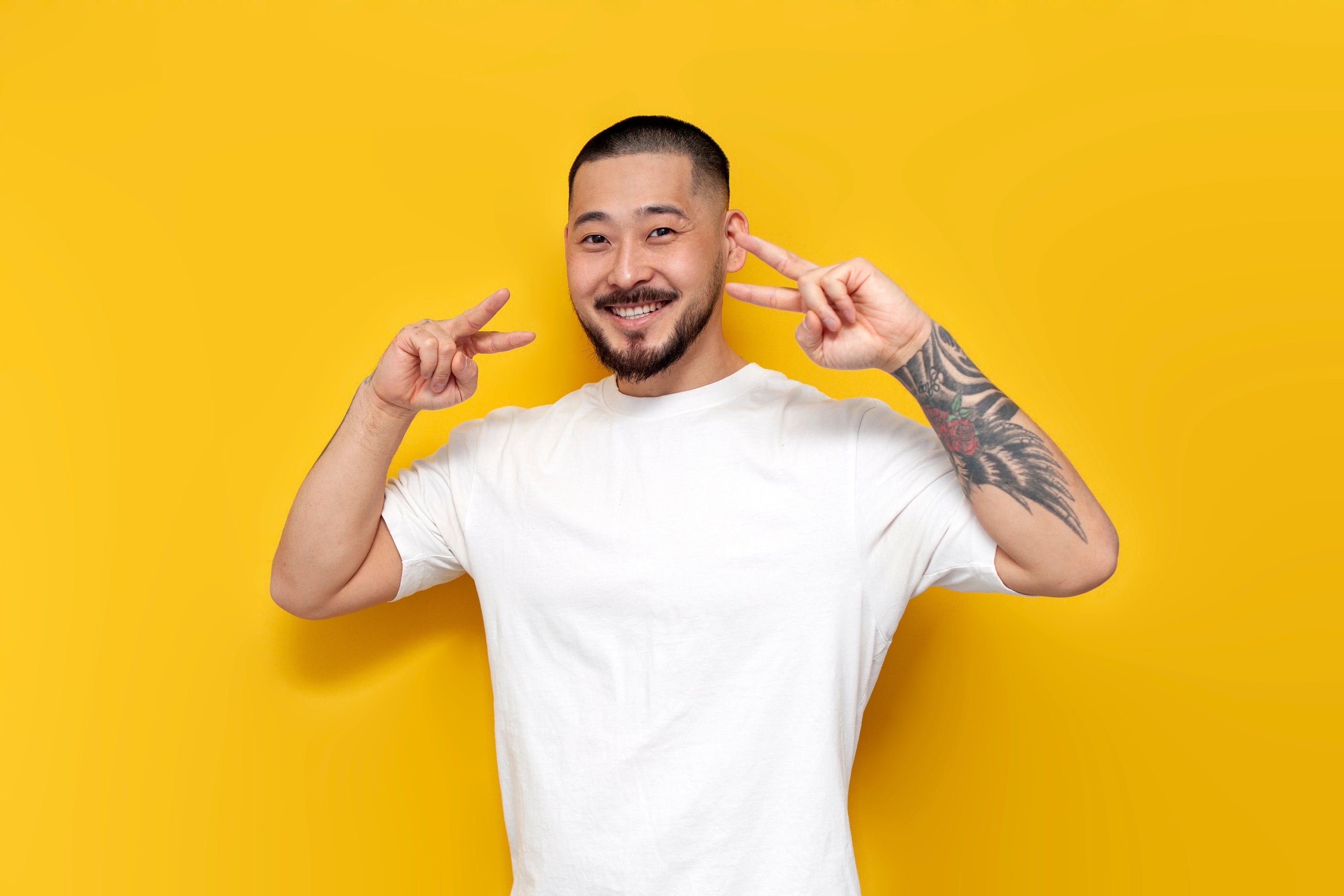 Smiling young man in a white t-shirt flashing peace signs against a bright yellow background, reflecting Supr Bueno’s modern, creative, and approachable web design studio for bold and emerging brands.